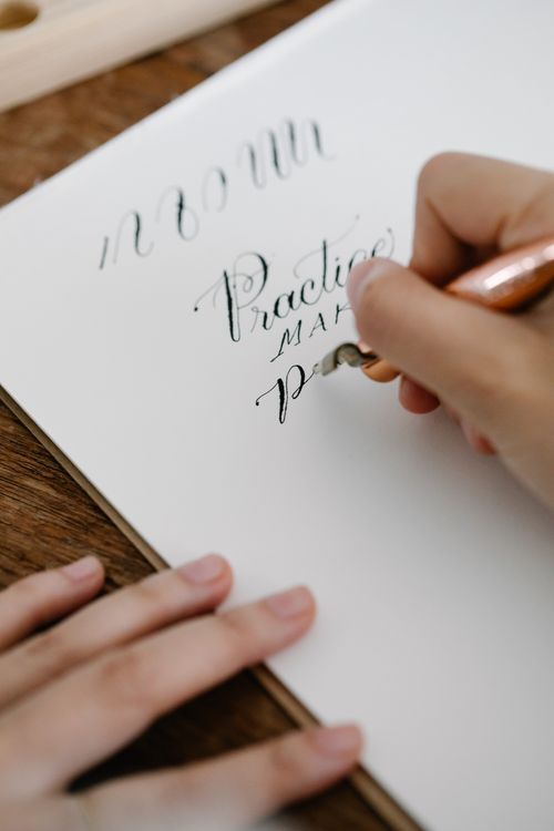 Hand practicing elegant calligraphy on white paper
