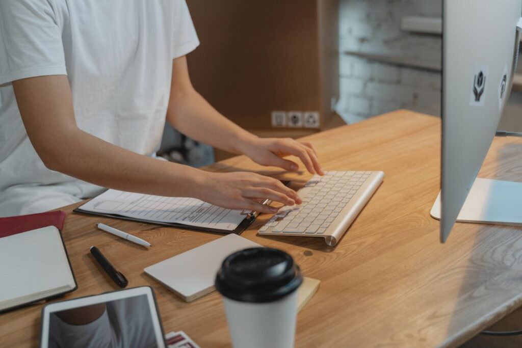 Person typing at a keyboard beside paperwork on a desk