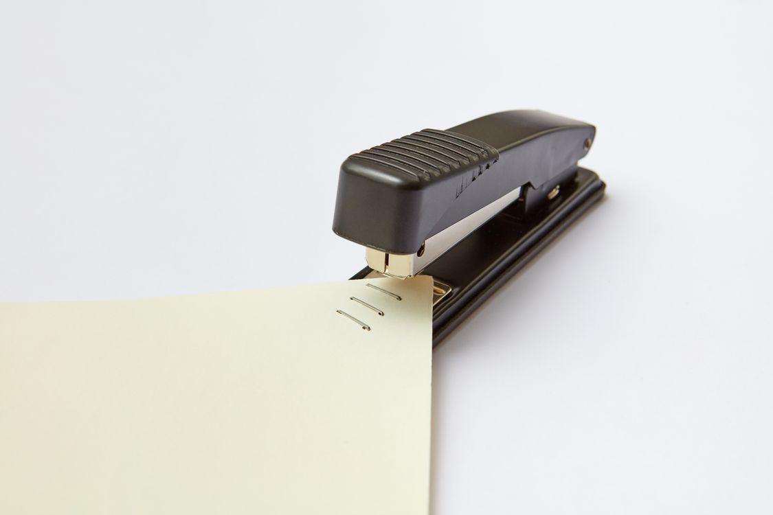 Close-up of a black stapler fastening a thick stack of papers