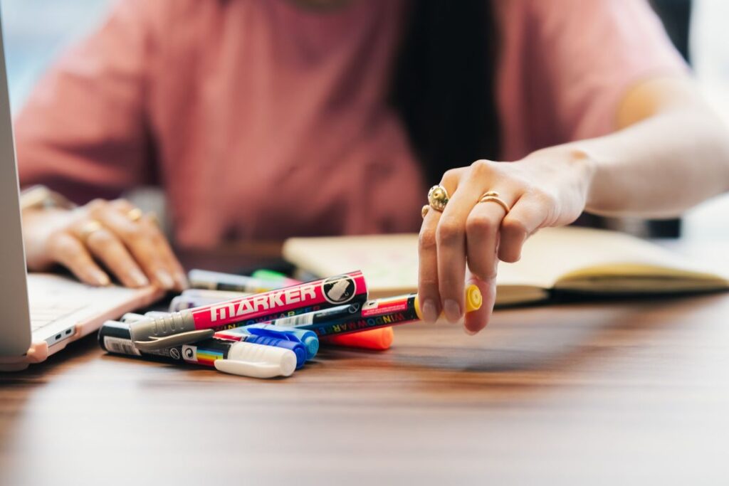 Hand selecting colorful marker pens from a bright office desk
