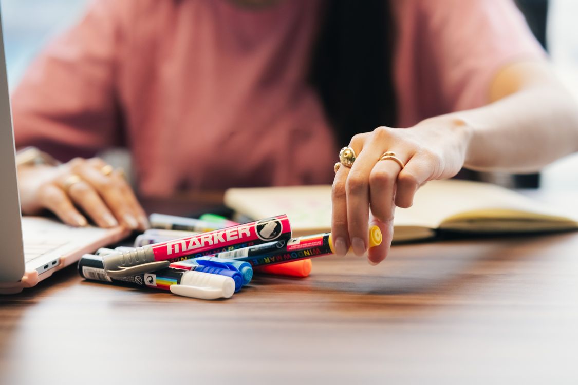 Hand selecting colorful marker pens from a bright office desk