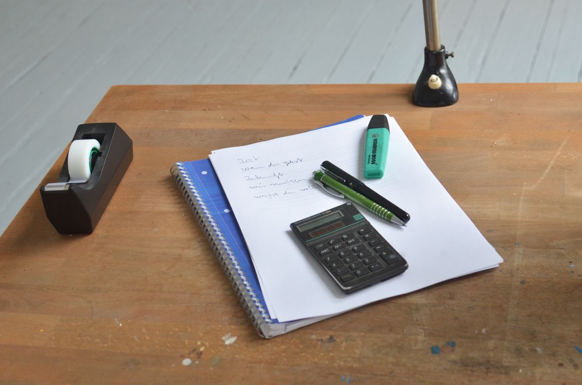 Office desk with a tape dispenser, calculator, notebook, and stationery
