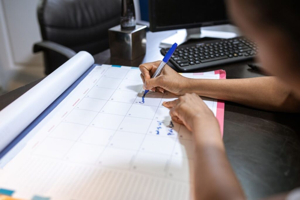 Person writing on a desk calendar while planning a schedule