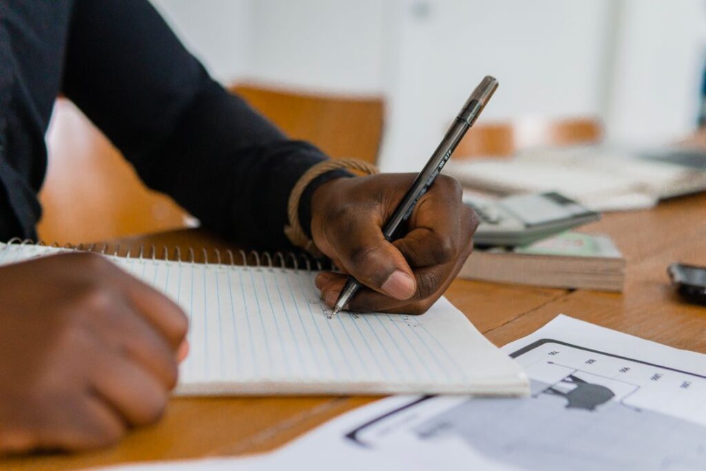 Left-handed person writing in a notebook at a wooden table