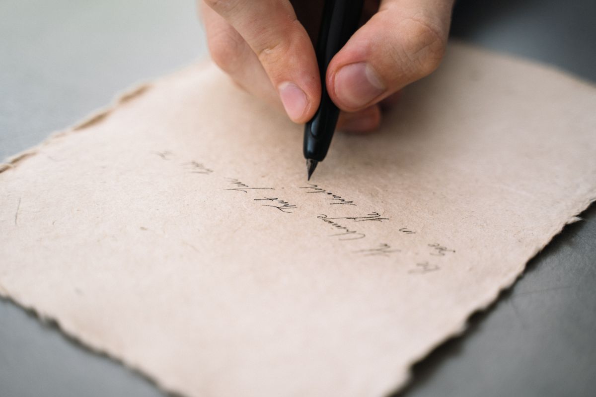 Close-up of a person writing with a black pen on textured letter paper